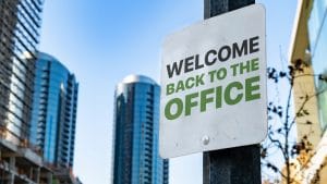 Sign reading “Welcome Back to the Office” against a backdrop of modern office towers, symbolizing the return-to-office movement.